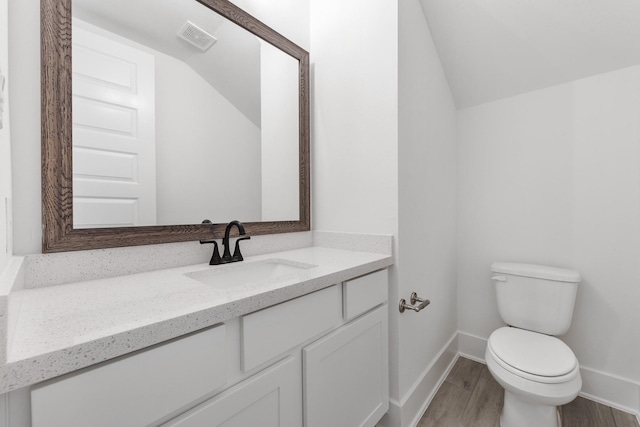 bathroom with visible vents, toilet, vaulted ceiling, vanity, and wood finished floors