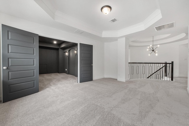 carpeted empty room featuring visible vents, a tray ceiling, a chandelier, and baseboards