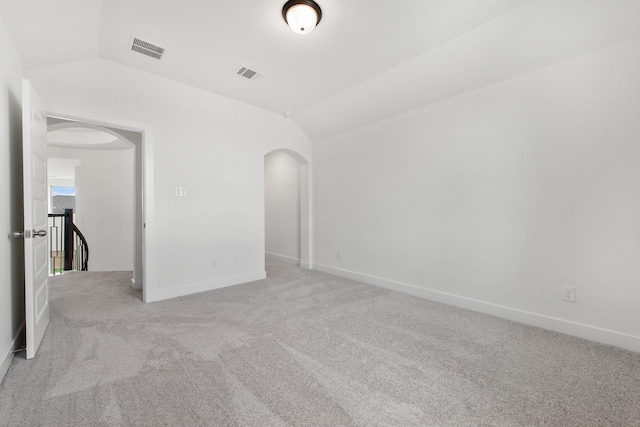 carpeted empty room featuring lofted ceiling, visible vents, and arched walkways