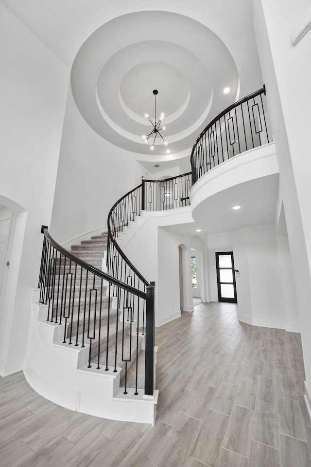 staircase with wood tiled floor, a high ceiling, a chandelier, and a tray ceiling