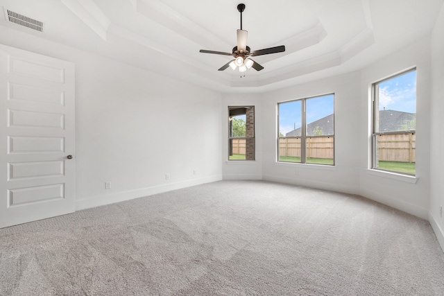 unfurnished room with carpet floors, a tray ceiling, plenty of natural light, and visible vents