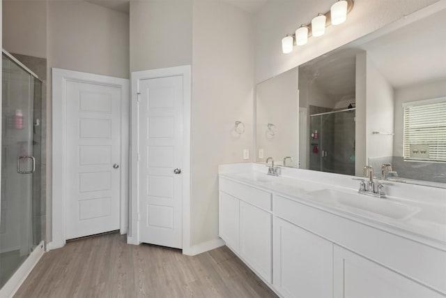 full bath with a stall shower, double vanity, a sink, and wood finished floors