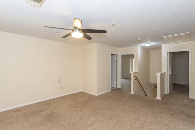 carpeted spare room featuring attic access, baseboards, visible vents, a ceiling fan, and a textured ceiling