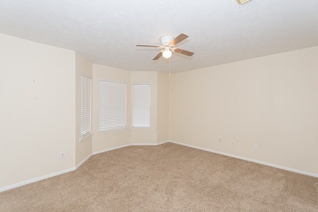 unfurnished room with light carpet, ceiling fan, a textured ceiling, and baseboards