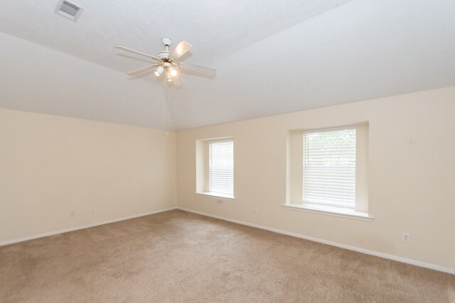 empty room with light carpet, lofted ceiling, visible vents, and a ceiling fan