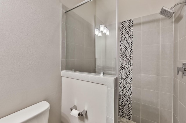 bathroom with toilet, tiled shower, and a textured wall