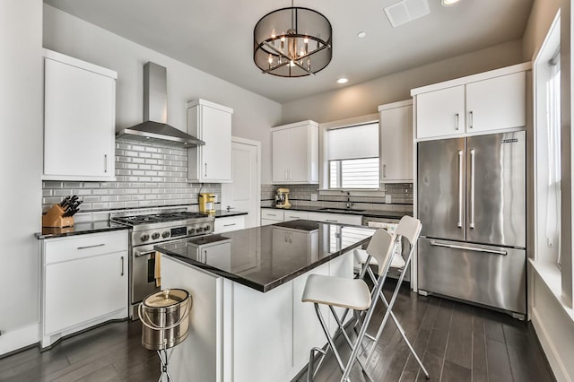 kitchen featuring high end appliances, dark countertops, a breakfast bar, wall chimney range hood, and a sink