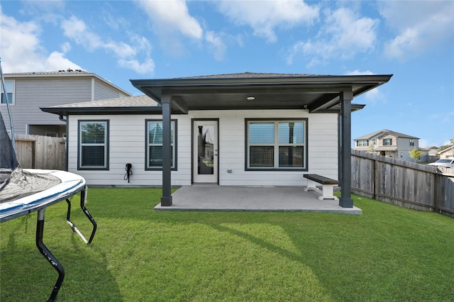 back of property featuring a fenced backyard, a yard, roof with shingles, a trampoline, and a patio area