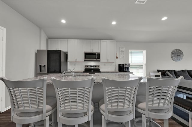 kitchen featuring decorative backsplash, dark wood-style flooring, light stone countertops, stainless steel appliances, and a sink