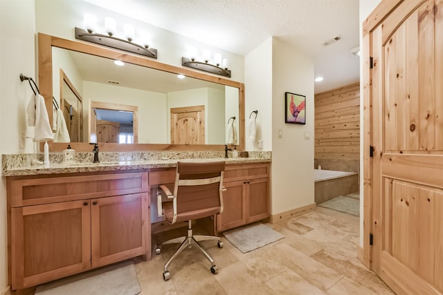 bathroom with double vanity, visible vents, a sink, a textured ceiling, and a bath