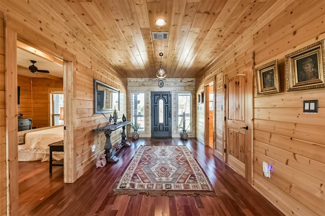 foyer entrance with wood ceiling, visible vents, wood walls, and dark wood-style flooring