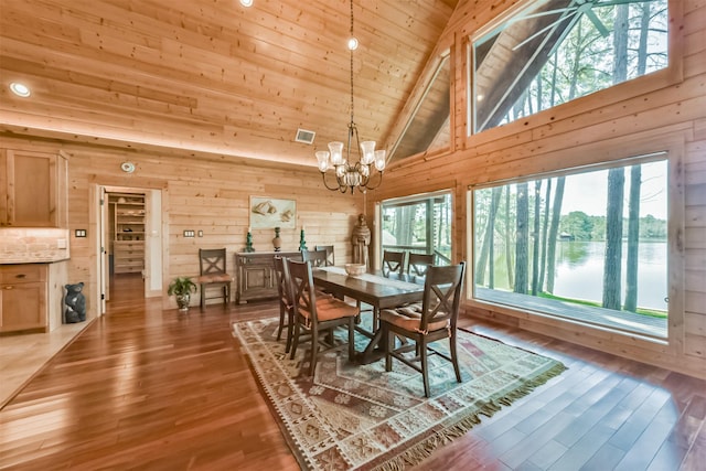 dining space featuring wood walls, an inviting chandelier, a water view, and a healthy amount of sunlight