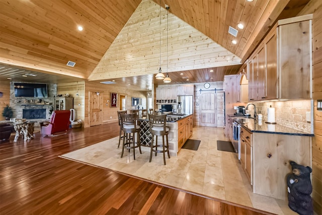 kitchen featuring light wood finished floors, visible vents, stainless steel fridge with ice dispenser, wood ceiling, and a fireplace