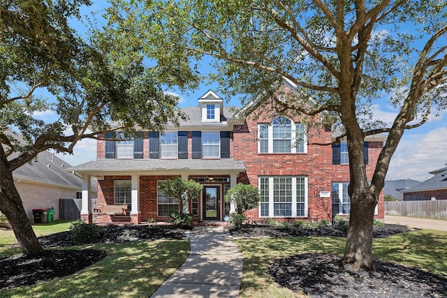 view of front facade with brick siding, a front yard, and fence