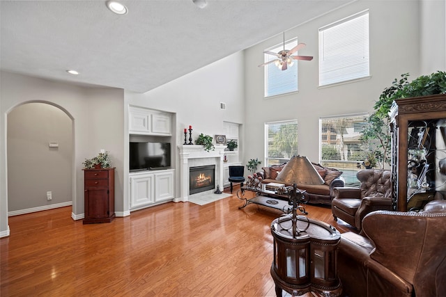 living room with light wood finished floors, arched walkways, baseboards, a ceiling fan, and a fireplace with flush hearth