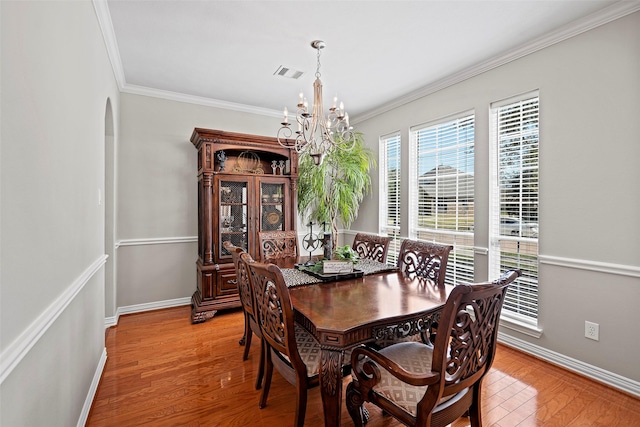 dining space featuring arched walkways, a notable chandelier, visible vents, light wood-style floors, and ornamental molding