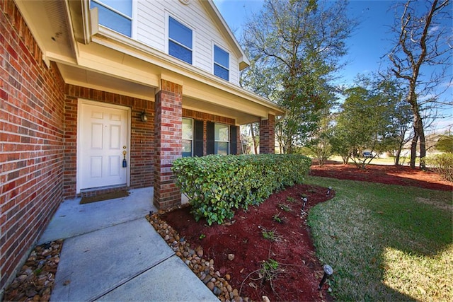 view of exterior entry featuring brick siding and a yard