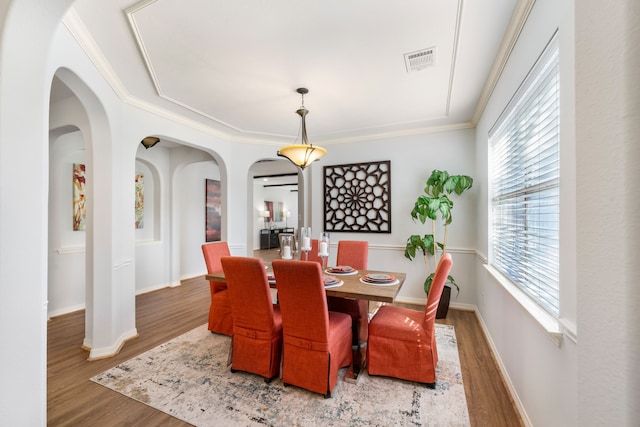 dining area featuring visible vents, ornamental molding, wood finished floors, arched walkways, and baseboards