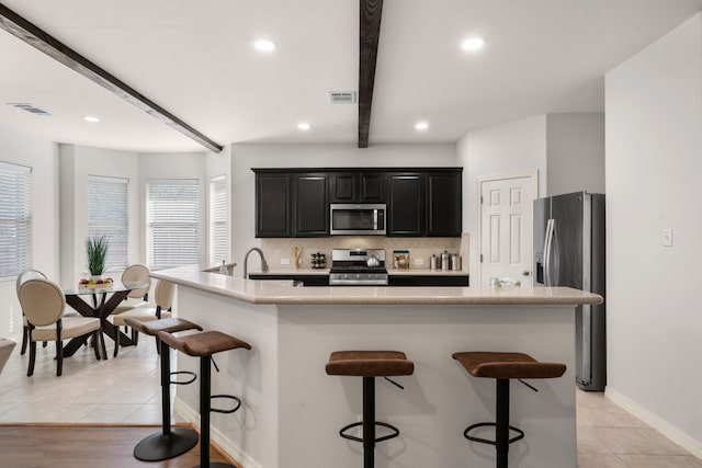 kitchen with visible vents, beam ceiling, stainless steel appliances, decorative backsplash, and dark cabinets