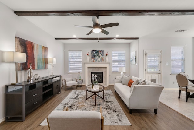 living room featuring a tiled fireplace, beam ceiling, wood finished floors, and baseboards