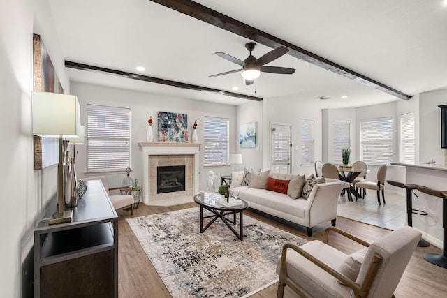 living area featuring a tiled fireplace, beam ceiling, recessed lighting, and light wood-style floors