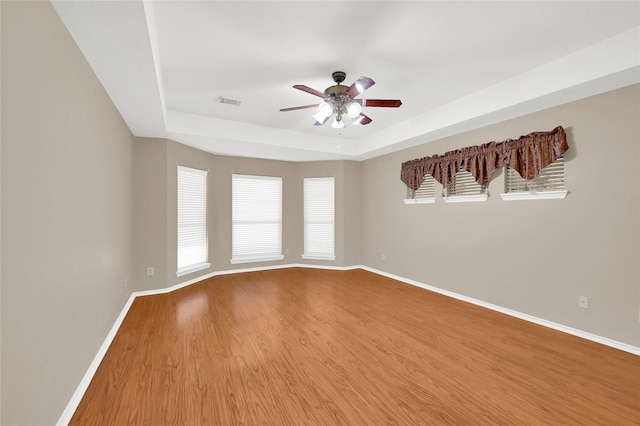 unfurnished room featuring ceiling fan, wood finished floors, visible vents, baseboards, and a tray ceiling