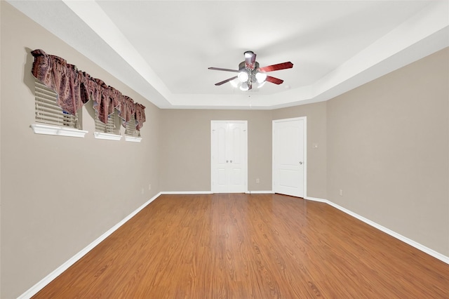 unfurnished bedroom with ceiling fan, light wood finished floors, a raised ceiling, and baseboards