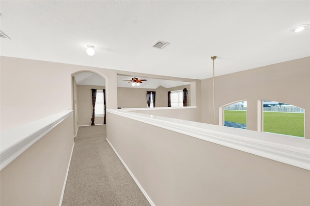 hallway featuring light carpet, a wealth of natural light, visible vents, and baseboards