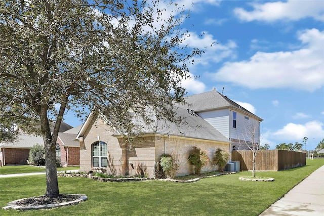 view of front of home featuring brick siding, roof with shingles, fence, central AC, and a front yard