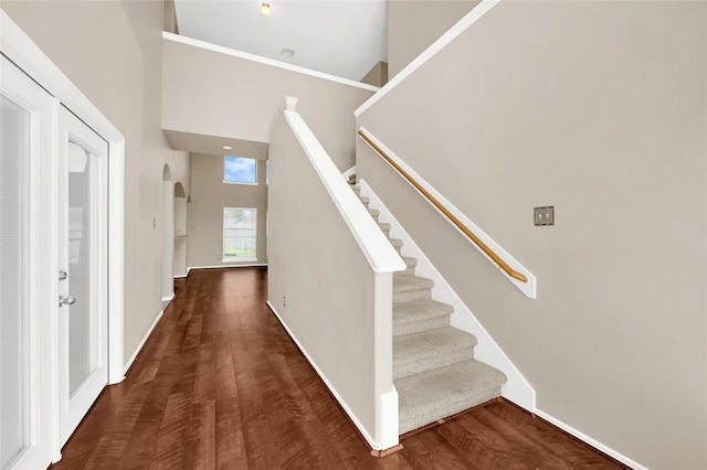 staircase featuring arched walkways, baseboards, a high ceiling, and wood finished floors