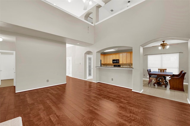 living area featuring ceiling fan, wood finished floors, arched walkways, and baseboards