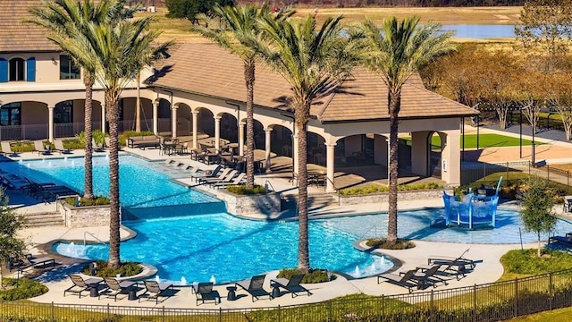 community pool with a water view, a patio area, and fence