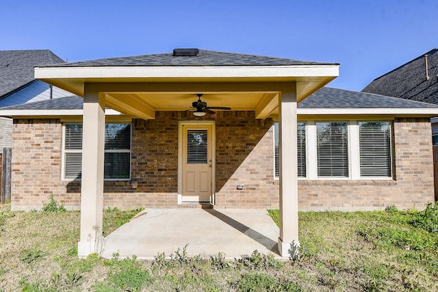 view of exterior entry with ceiling fan, a patio, a shingled roof, and brick siding