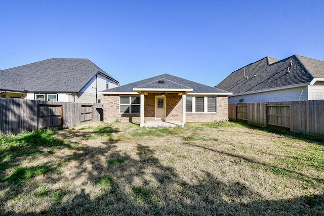 rear view of house featuring a shingled roof, a fenced backyard, and brick siding