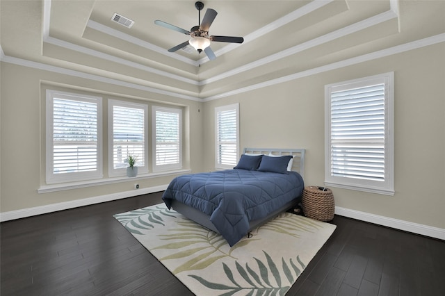 bedroom with baseboards, visible vents, a tray ceiling, dark wood-type flooring, and crown molding