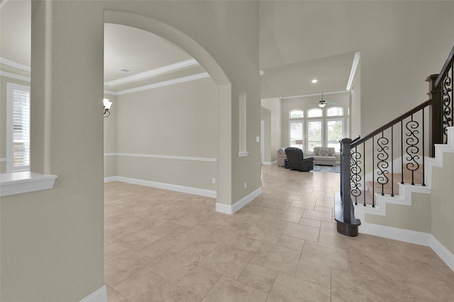 foyer featuring stairs, crown molding, arched walkways, and baseboards