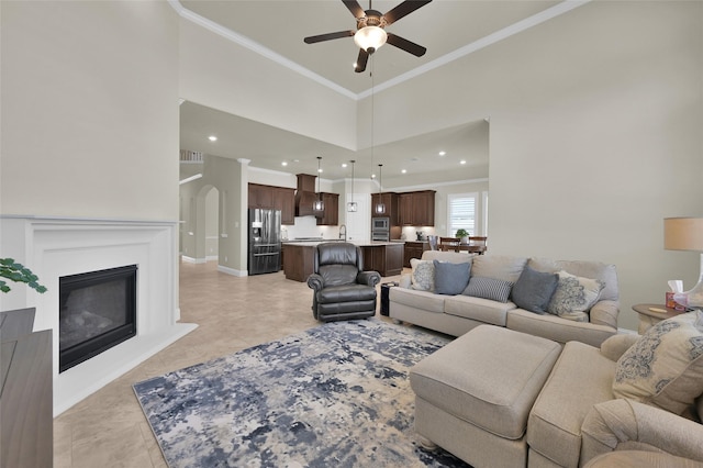 living room with arched walkways, a glass covered fireplace, a towering ceiling, and ornamental molding