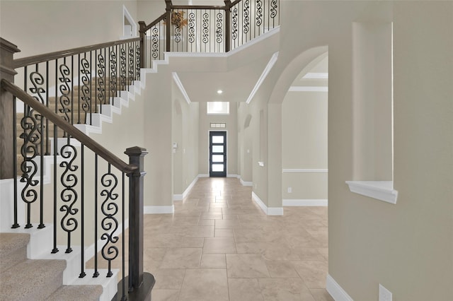 foyer with crown molding, arched walkways, baseboards, and a towering ceiling