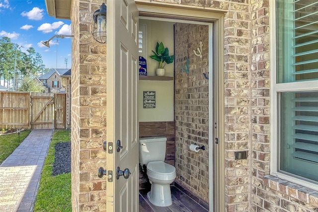 bathroom featuring toilet and brick wall