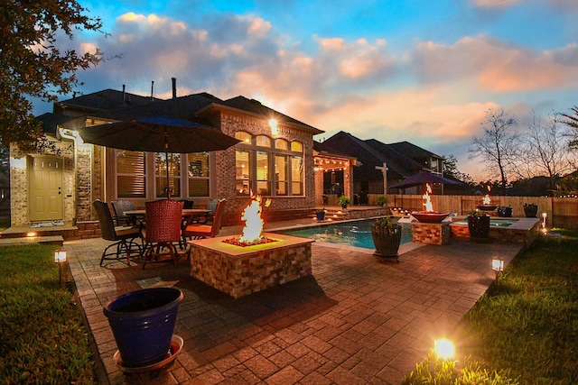 pool at dusk with area for grilling, a pool with connected hot tub, a fenced backyard, an outdoor fire pit, and a patio area