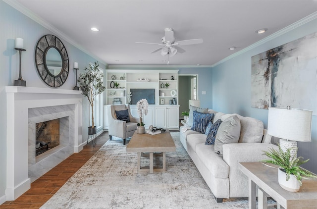 living area featuring recessed lighting, ornamental molding, a high end fireplace, a ceiling fan, and wood finished floors