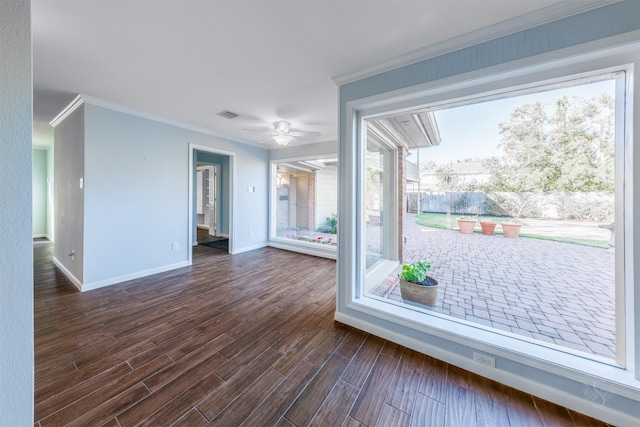 empty room with crown molding, dark wood finished floors, visible vents, a ceiling fan, and baseboards