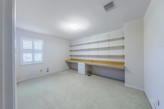 unfurnished office with light colored carpet, built in study area, visible vents, and baseboards