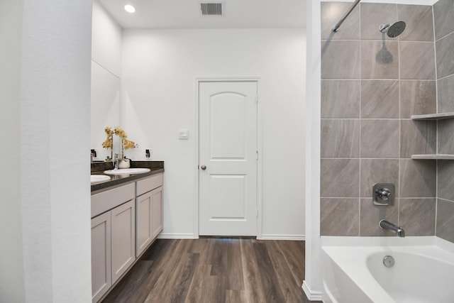 bathroom featuring double vanity, visible vents, wood finished floors, washtub / shower combination, and a sink