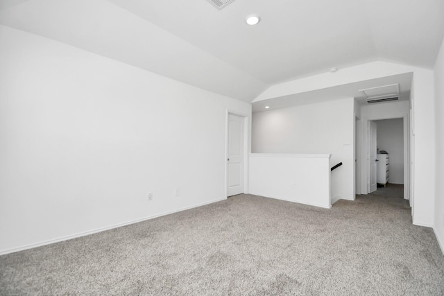 carpeted spare room with vaulted ceiling, separate washer and dryer, attic access, and baseboards