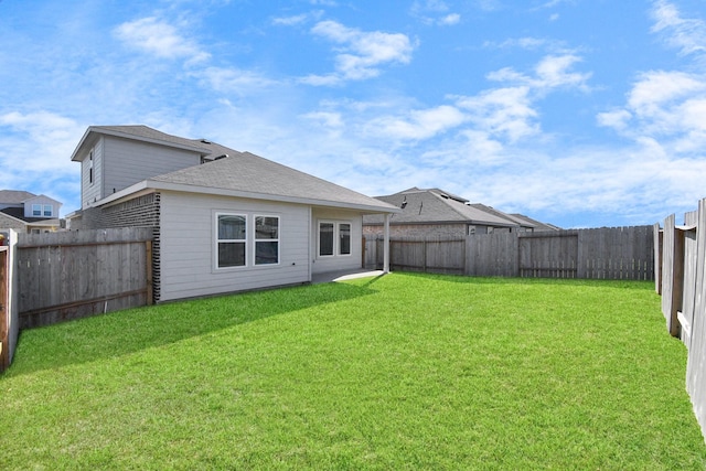 back of house featuring roof with shingles, a lawn, and a fenced backyard