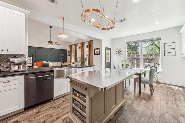 kitchen featuring lofted ceiling, visible vents, stainless steel dishwasher, a sink, and wood finished floors