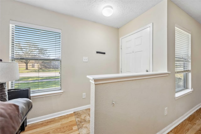 foyer with a wealth of natural light, a textured ceiling, baseboards, and wood finished floors