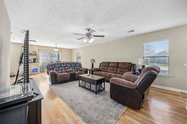 living area featuring light wood finished floors, baseboards, visible vents, and a textured ceiling