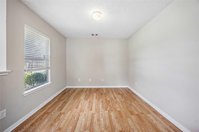 empty room with a textured ceiling, light wood finished floors, visible vents, and baseboards